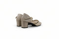 A pair of women's block-heel sandals in beige faux leather with a woven beige and gold pattern on the toe strap, shown from a side-rear angle against a light gray studio background.
