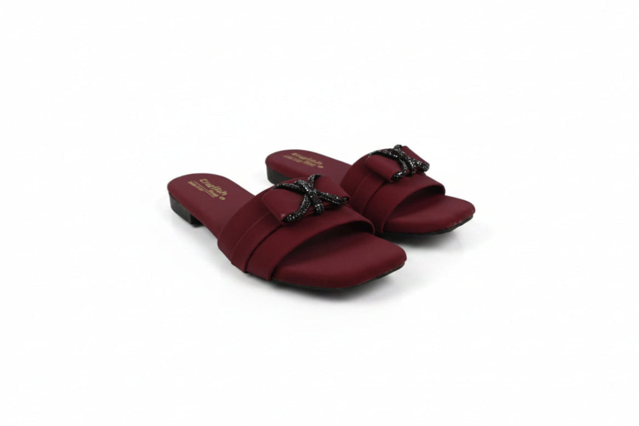 A pair of women's open-toe slide sandals in burgundy with black star-shaped embellishments on the straps, photographed on a light gray studio background.