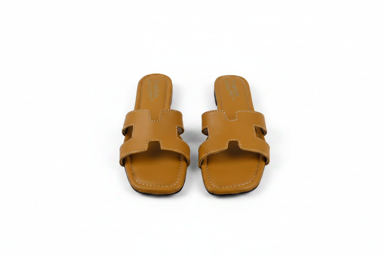 A pair of tan leather slide sandals with a double strap design, photographed from above on a light gray fabric background.