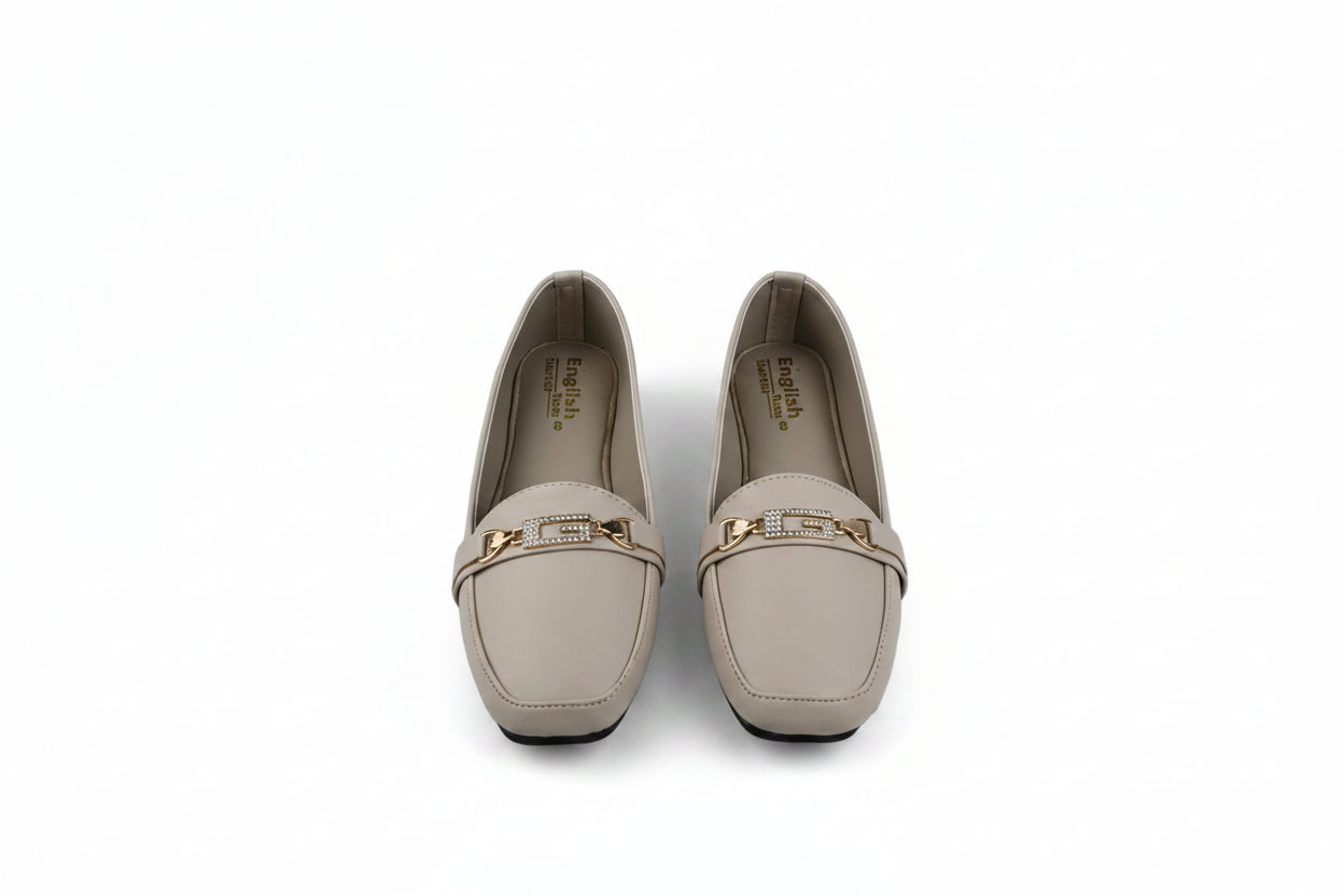 A pair of beige leather loafers with a gold-tone metal bar detail across the vamp, shown on a light gray background.