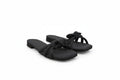 A pair of black slide sandals with knotted strap details, photographed on a light gray fabric backdrop.