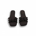 A pair of dark brown slide sandals with knotted bow details across the toes, shown on a light gray background.