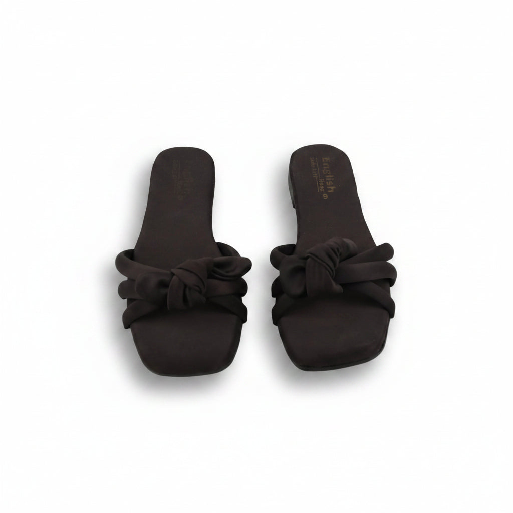 A pair of dark brown slide sandals with knotted bow details across the toes, shown on a light gray background.