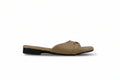 A single tan leather slide sandal with a low black heel and a small gold buckle detail on the strap, shown in profile against a light gray background.