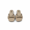 A pair of beige slide sandals with gold-tone horsebit hardware and rhinestone accents, displayed on a light gray surface.
