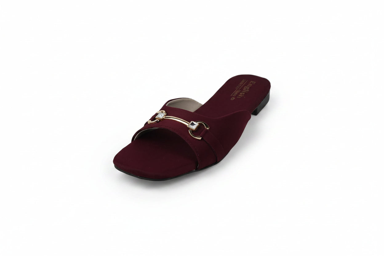 A single burgundy open-toe flat sandal with a gold horsebit detail across the instep, photographed on a light gray textured background.