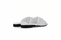 A pair of white slide sandals with perforated straps and black soles, photographed on a light gray floor against a matching gray background.