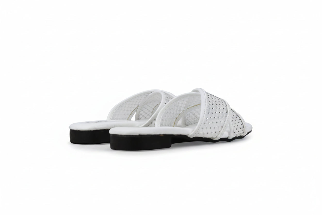 A pair of white slide sandals with perforated straps and black soles, photographed on a light gray floor against a matching gray background.