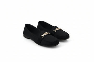 A pair of black slip-on flats with a gold-tone decorative chain link detail across the vamp, displayed on a light gray studio background.