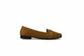 A single tan leather loafer flat with a small gold-tone buckle detail on the vamp, photographed from the side against a light gray studio backdrop.