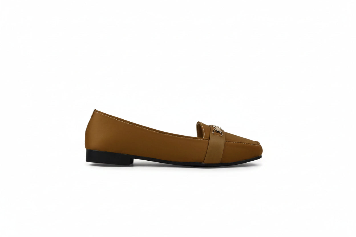 A single tan leather loafer flat with a small gold-tone buckle detail on the vamp, photographed from the side against a light gray studio backdrop.