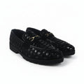 A pair of black woven leather loafers with a gold-tone horsebit detail on the strap, displayed against a light gray fabric backdrop.