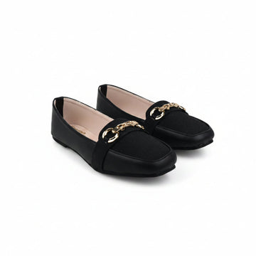 A pair of black flat loafers with a gold-tone double-ring chain detail across the vamp, displayed on a light gray fabric background.