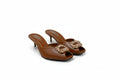 A pair of women's brown leather mule heels with high stiletto heels and a jeweled floral embellishment across the peep-toe front, displayed on a light gray studio background.