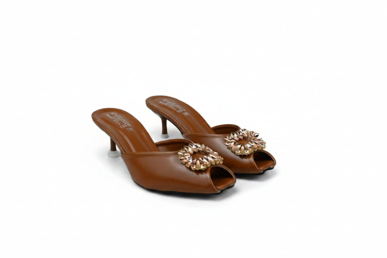 A pair of women's brown leather mule heels with high stiletto heels and a jeweled floral embellishment across the peep-toe front, displayed on a light gray studio background.