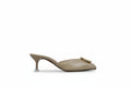 A single beige leather mule high-heel shoe with a pointed toe and a gold-tone metal logo clasp, shown in profile against a textured light gray background.