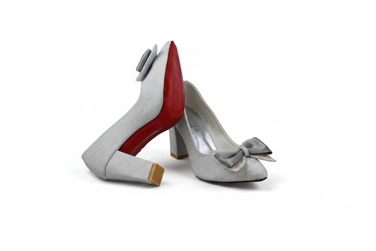 A pair of women's high-heeled pumps in a light silver-gray textured fabric, featuring a pointed toe, a decorative gray bow on the side, and a signature red outsole, displayed against a white studio backdrop.