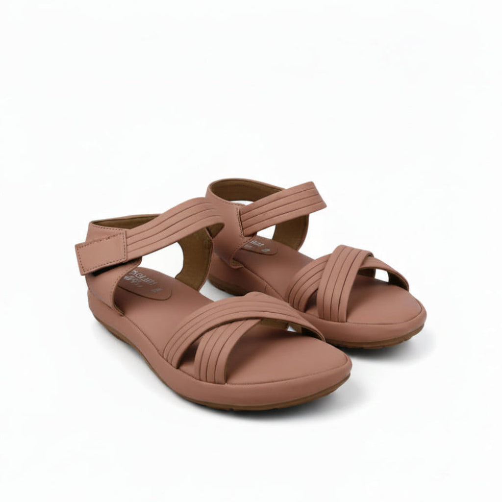 A pair of women's flat sandals in a dusty rose or mauve color, featuring criss-cross front straps and an adjustable ankle strap, shown on a light gray fabric background.