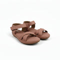 A pair of women's flat sandals in a dusty rose or mauve color, featuring criss-cross front straps and an adjustable ankle strap, shown on a light gray fabric background.
