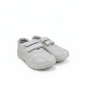 A pair of white children's low-top sneakers with double hook-and-loop straps, shown on a light gray textured studio background.