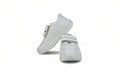 A pair of white low-top casual shoes with double hook-and-loop strap closures, displayed on a light gray studio background.