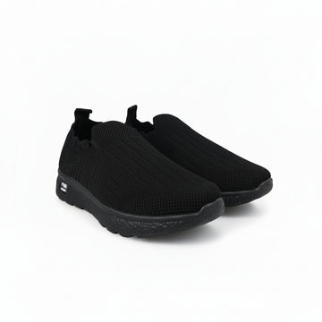 A pair of black slip-on knit sneakers with textured soles, displayed on a light gray background.