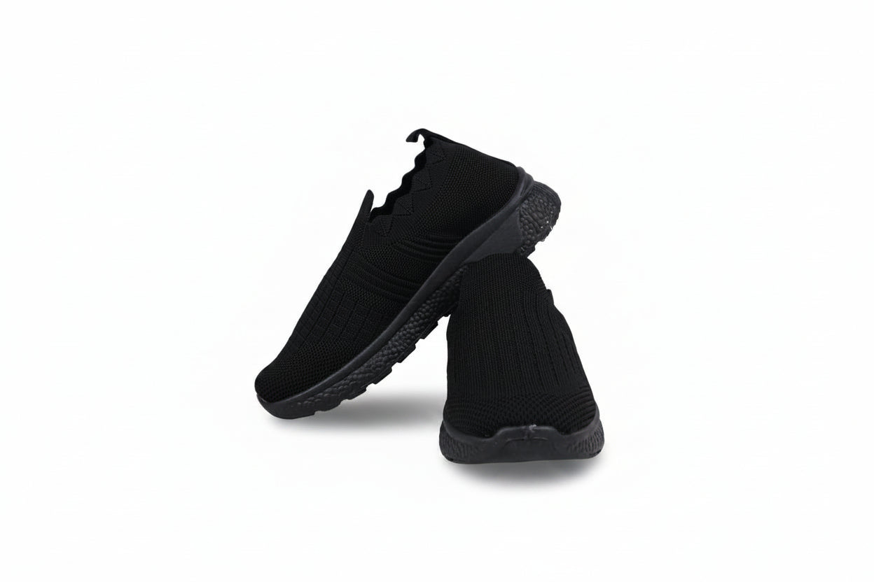 A pair of black slip-on knit sneakers with black soles, displayed against a light gray studio background.