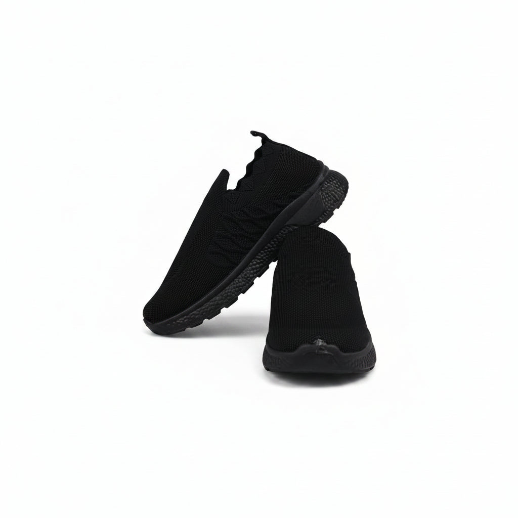 A pair of black slip-on athletic sneakers with a textured knit upper and chunky black soles, displayed against a light gray studio background.