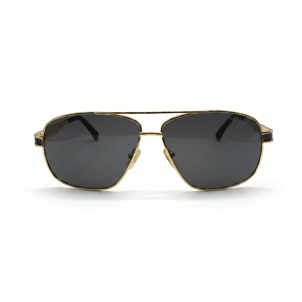 A pair of classic aviator sunglasses with a gold metal frame and dark gray lenses, displayed on a white surface with two silver studio reflectors in the background.