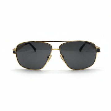 A pair of classic aviator sunglasses with a gold metal frame and dark gray lenses, displayed on a white surface with two silver studio reflectors in the background.