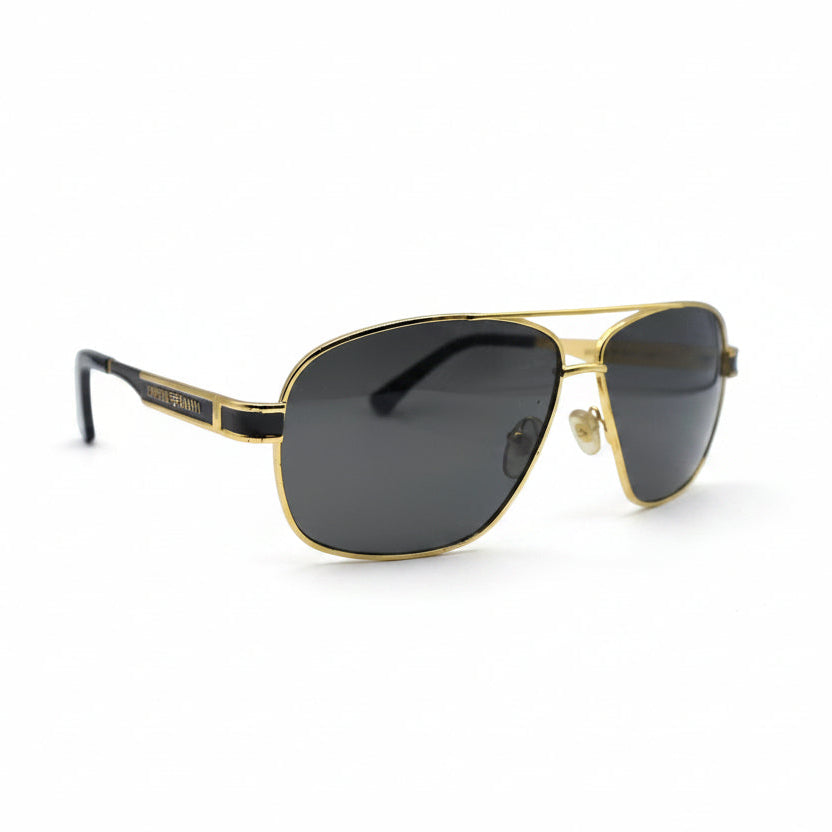 A pair of classic aviator sunglasses with a gold metal frame and dark gray lenses, displayed on a white surface with two silver studio reflectors in the background.