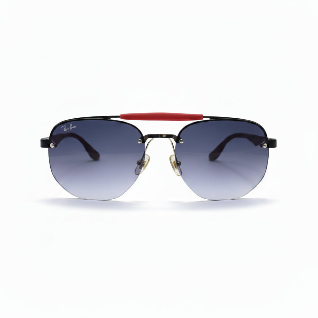 Ray-Ban aviator sunglasses with a black metal frame, gradient gray lenses, and a signature red bridge, displayed on a white surface with softbox lights in the background.