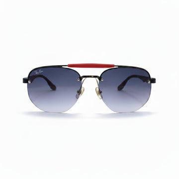 Ray-Ban aviator sunglasses with a black metal frame, gradient gray lenses, and a signature red bridge, displayed on a white surface with softbox lights in the background.