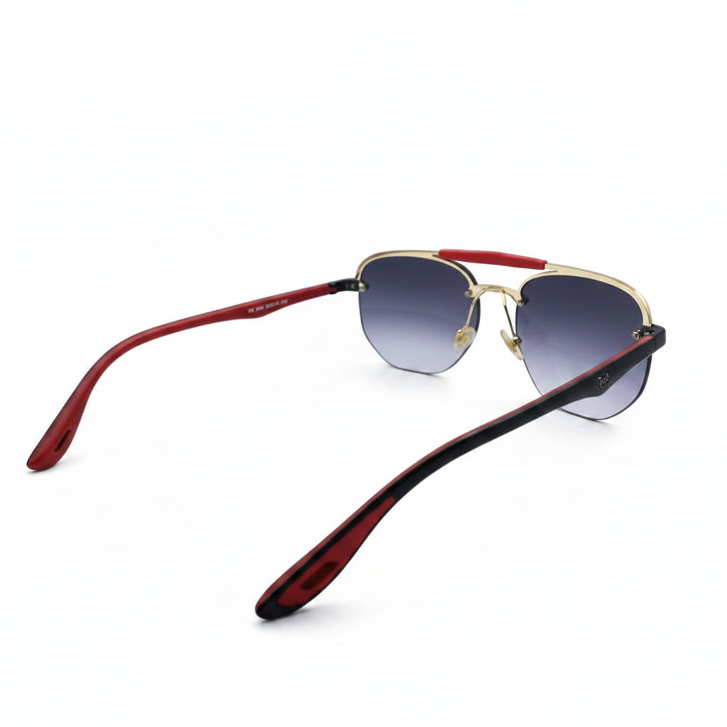 Ray-Ban aviator sunglasses with a black metal frame, gradient gray lenses, and a signature red bridge, displayed on a white surface with softbox lights in the background.