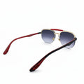A pair of aviator-style sunglasses with gradient purple lenses, gold metal frames, and red temples, displayed on a white surface with a reflective silver backdrop.