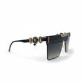 A pair of designer sunglasses with a black acetate frame, gold-tone metal accents, and gradient lenses, displayed on a white surface between two silver studio reflectors.