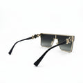 A pair of square-frame sunglasses with black temples, gold metal rims, and gradient dark lenses, displayed on a white surface with a reflective silver backdrop.