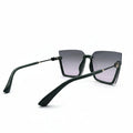 A pair of square-frame sunglasses with a matte black frame and dark gray-to-pink gradient lenses, displayed on a white surface between two silver studio reflector panels.