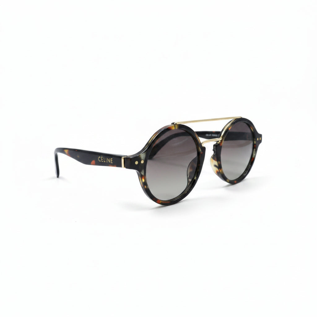 Round sunglasses with a tortoiseshell pattern, a thin gold metal bridge, and gradient brown lenses, displayed on a white surface between two silver studio reflectors.