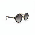Celine round sunglasses with a tortoiseshell pattern, gold metal double bridge, and gradient gray lenses, displayed on a white surface between two gray reflective studio panels.