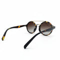Oversized round sunglasses with tortoiseshell acetate frames and gradient brown lenses, displayed on a white surface between two textured silver panels.
