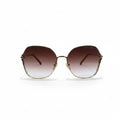 Oversized square sunglasses with a gold metal frame and brown gradient lenses, displayed on a white surface with a reflective silver backdrop.