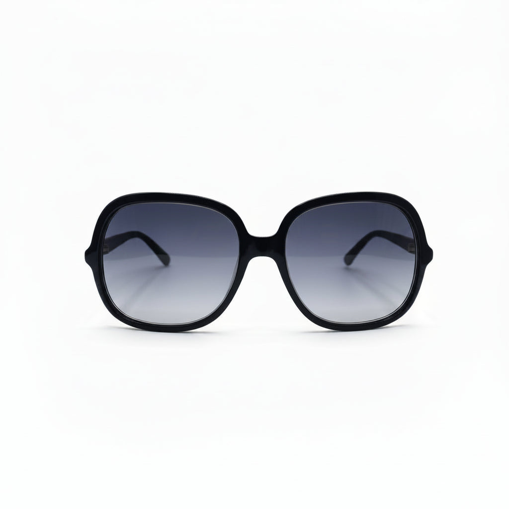Oversized square sunglasses with a thick black frame and dark gradient lenses, displayed on a white surface with two textured silver props on either side.