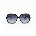 Oversized square sunglasses with a thick black frame and dark gradient lenses, displayed on a white surface with two textured silver props on either side.
