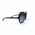 A pair of black cat-eye sunglasses with dark gray lenses, displayed on a white surface between two silver studio reflectors.