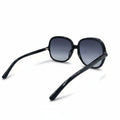 Black oversized square sunglasses with gradient gray lenses, displayed on a white surface with textured silver stands in the background.