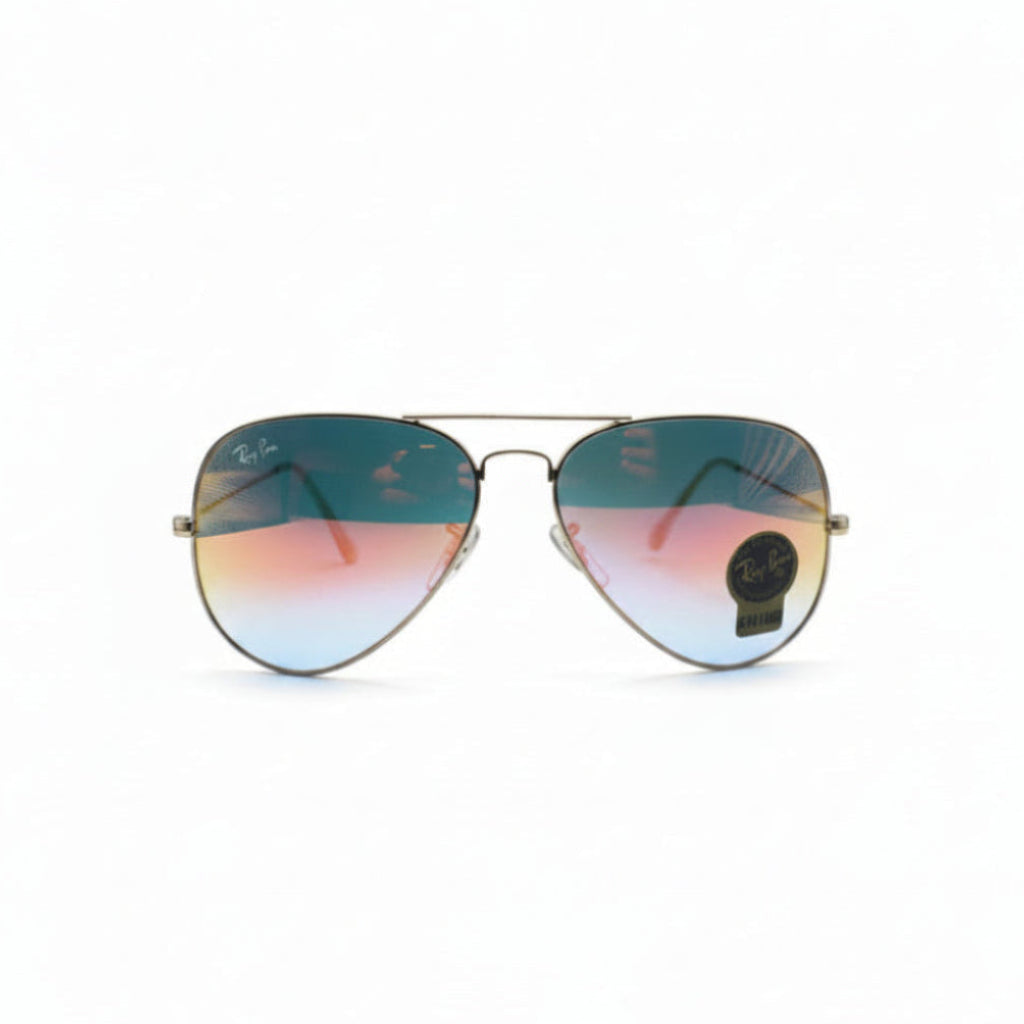 A pair of aviator sunglasses with a gold metal frame and gradient lenses shifting from teal-blue to pink-orange, displayed on a white surface between two textured silver panels.