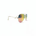 A pair of aviator-style sunglasses with gold metal frames and reflective lenses showing a yellow-to-blue gradient, displayed on a white surface between two dark gray studio lights.