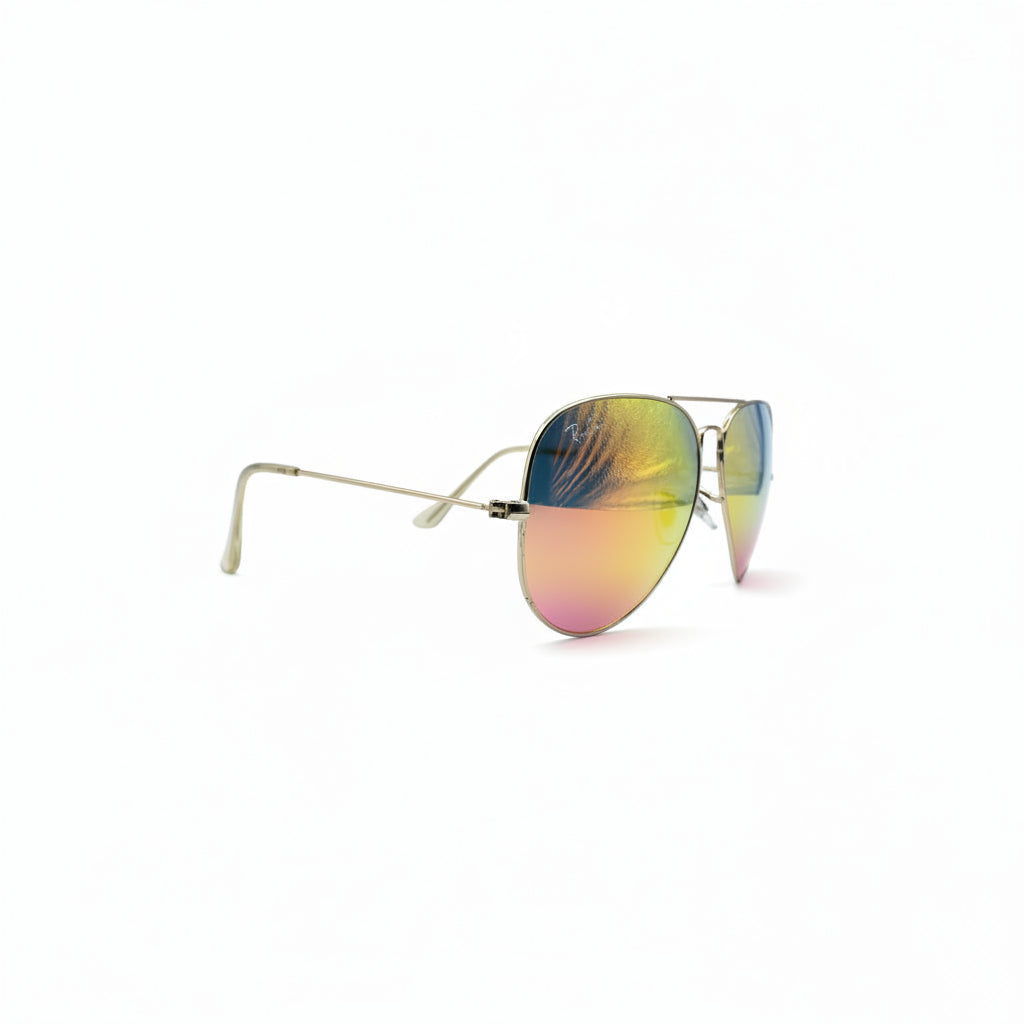 A pair of aviator-style sunglasses with gold metal frames and reflective lenses showing a yellow-to-blue gradient, displayed on a white surface between two dark gray studio lights.