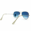 A pair of aviator sunglasses with gold metal frames and blue-to-turquoise gradient lenses, displayed on a white surface with a reflective silver backdrop.